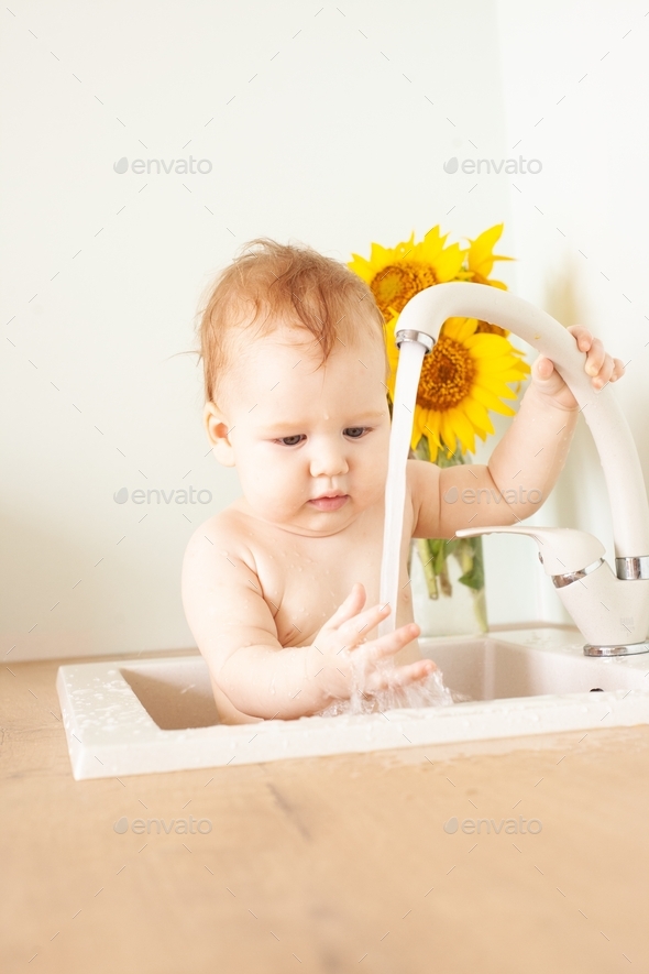 Baby taking bath in kitchen sink. Little boy bathing. Water fun for