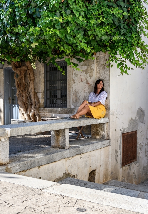 Young woman relaxing in shade of tree in old town.