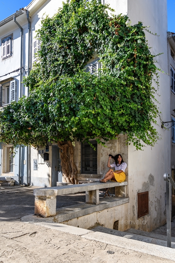 Young woman relaxing in shade of tree in old town.