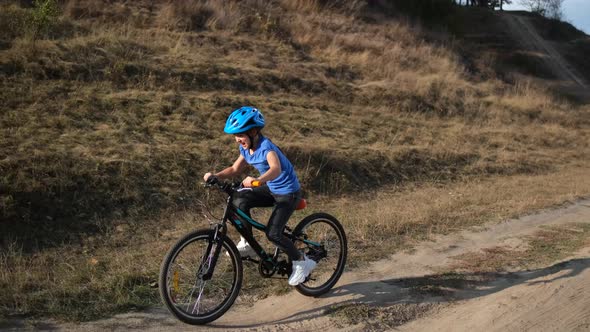 A little girl rides a Bicycle in a protective helmet near a hill in nature.