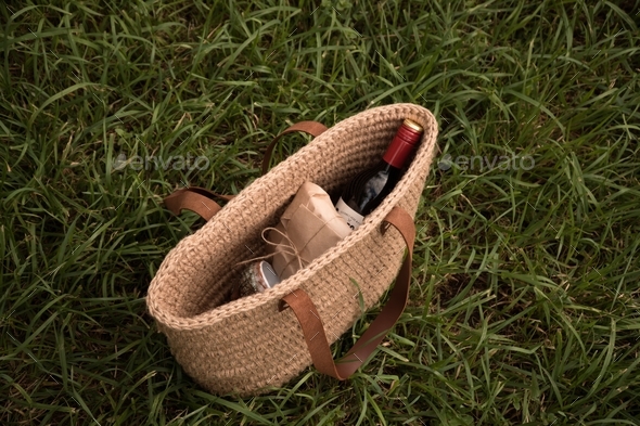 Jute basket with wine and cheese on grass for picnic