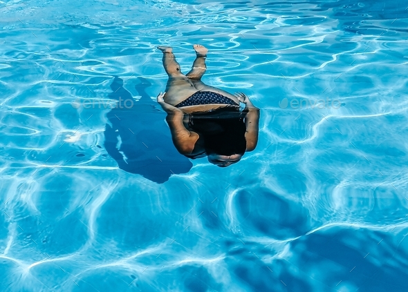 Young woman in bikini swimming underwater in pool on sunny day in summer.