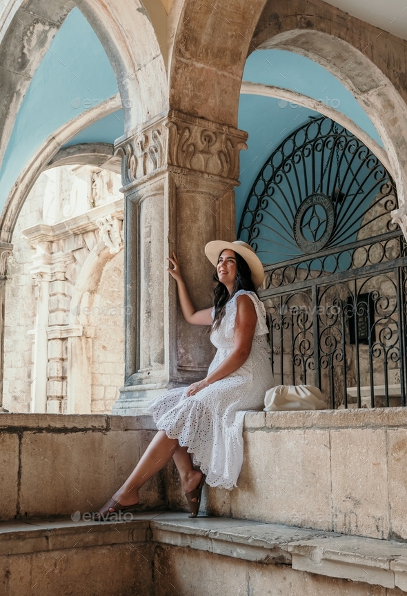 Full length lifestyle portrait of attractive young woman sitting under arched columns