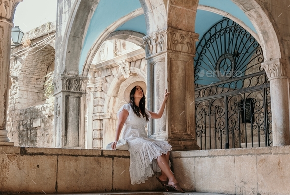 Full length lifestyle portrait of attractive young woman sitting under arched columns
