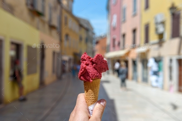 Personal perspective photo of hand holding delicious gelato in cone in street of colorful town