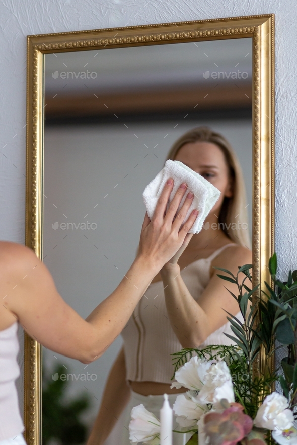 young girl cleans the house. He wipes the mirror with a napkin.