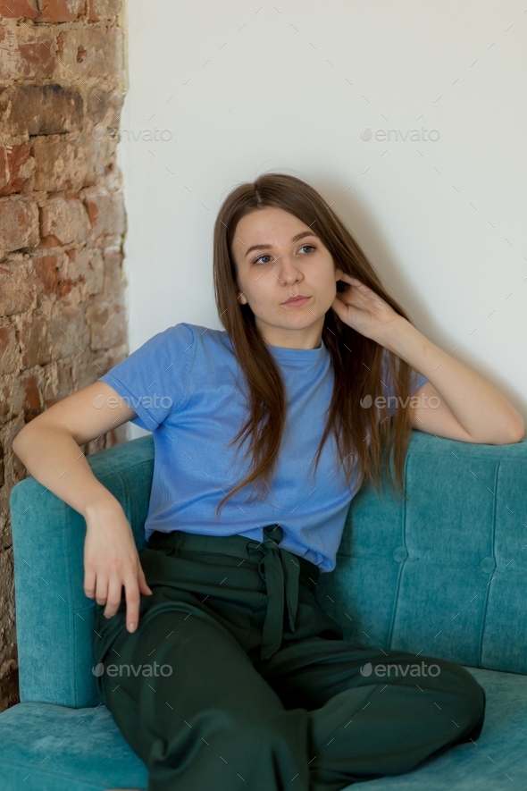 a girl in a blue t-shirt and green trousers sits on a sofa in a room, studio, office