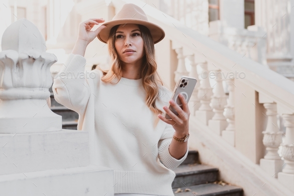 stylish elegant woman in dress and sweater in felt hat posing on the steps of beautiful, retro build