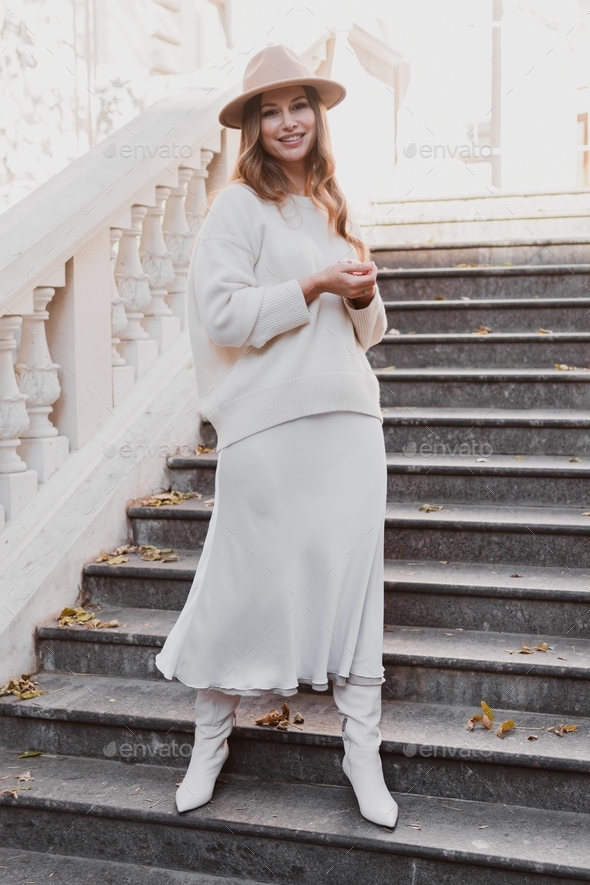 stylish elegant woman in dress and sweater in felt hat posing on the steps of beautiful, retro build