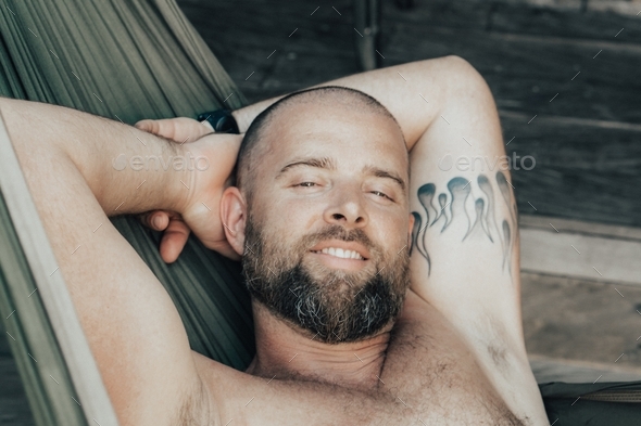 Bearded and tattooed man smiling laying in the hammock