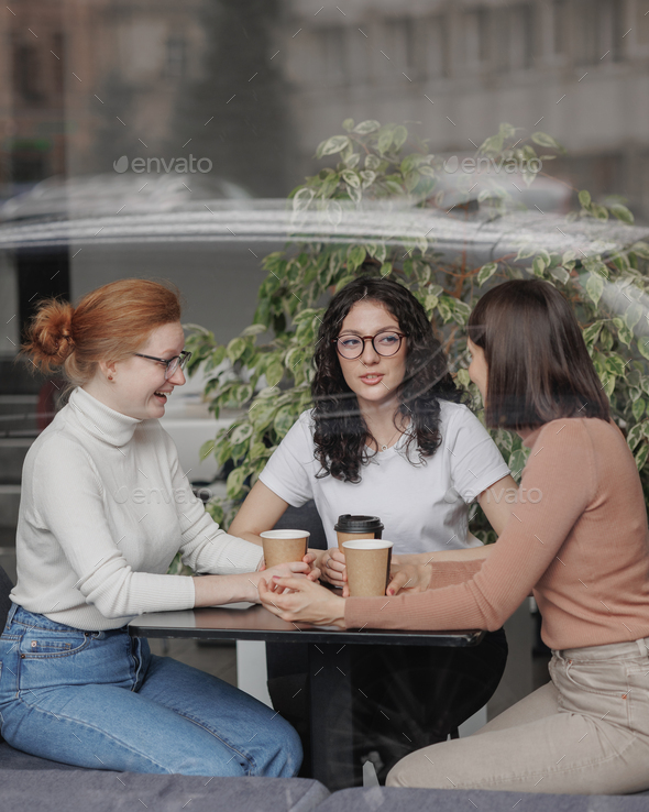 three female friends are talking in a coffee shop and drinking tea, moral support and caring