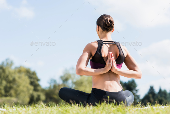 young yogini in Reverse Prayer Pose practicing yoga outdoors