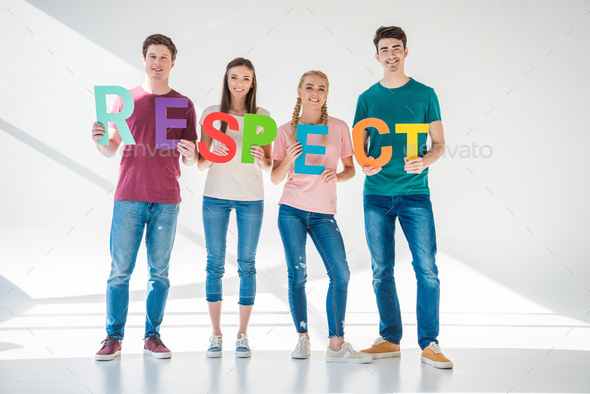 full length view of happy young friends holding colorful word respect and smiling at camera on grey