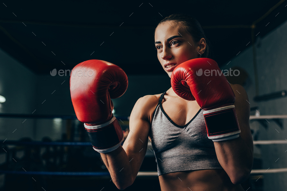 young sportswoman in boxing gloves training on boxing ring