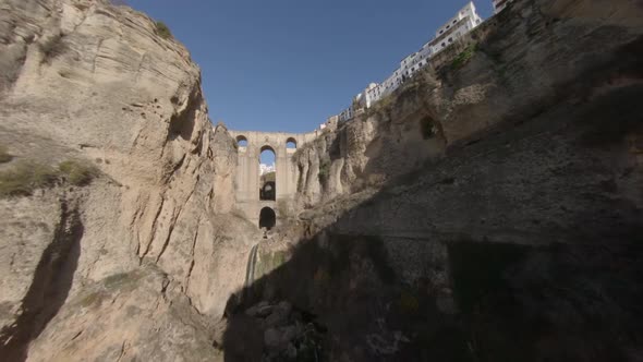 Slow aerial flight up deep gorge toward medieval arch bridge in Spain alt