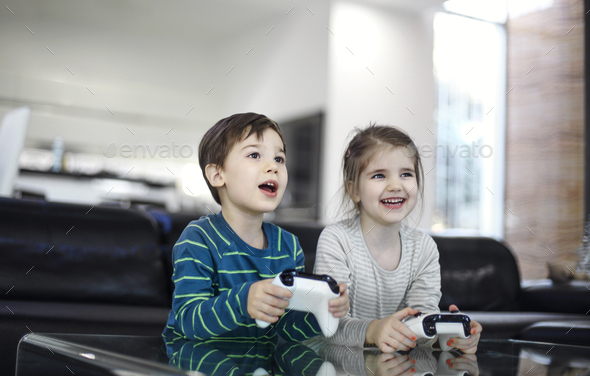 Joyful children with game controllers play video games at home