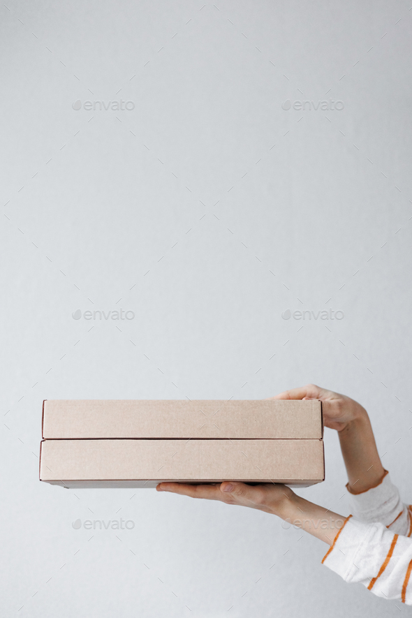 women\'s hands hold cardboard boxes on a gray background. food and drink delivery. biodegradable