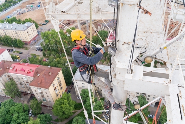 A worker with climbing equipment serves a city TV tower. Work at a high-rise facility.