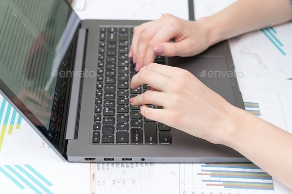 Cropped female hands typing text on a laptop keyboard close-up