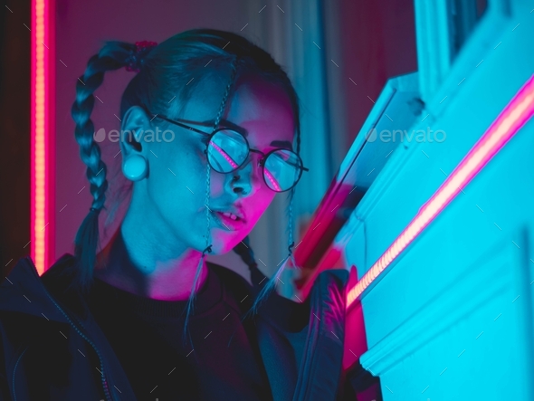 Young pretty girl with unusual hairstyle near me glowing pink and blue neon lights of the city