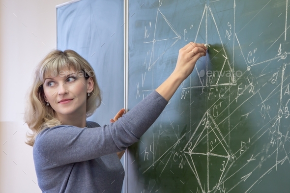 Young woman teacher writes on the blackboard with chalk closeup