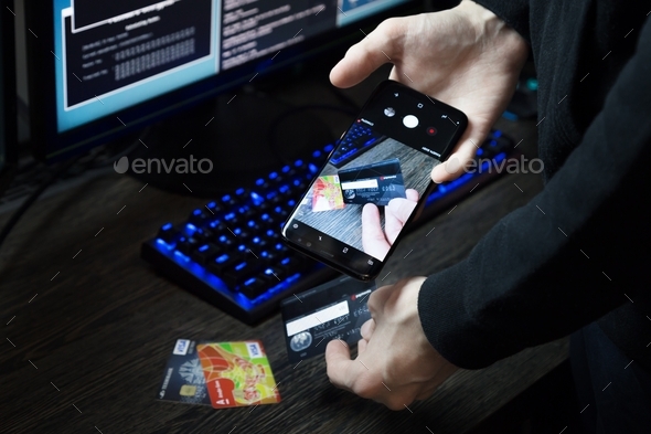 A hacker sits in front of a computer and scans the codes of payment cards using his phone