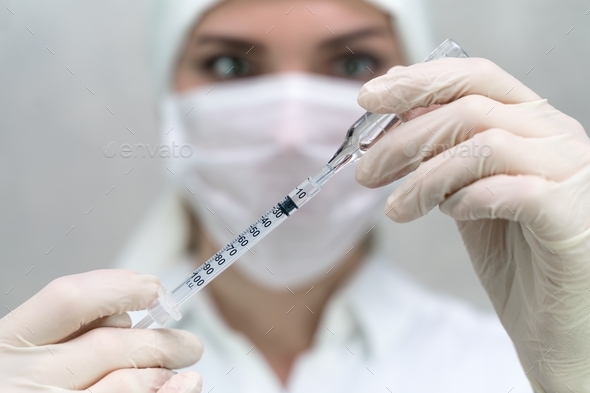 The nurse draws the medicine into an injection syringe. Close-up and soft focus.