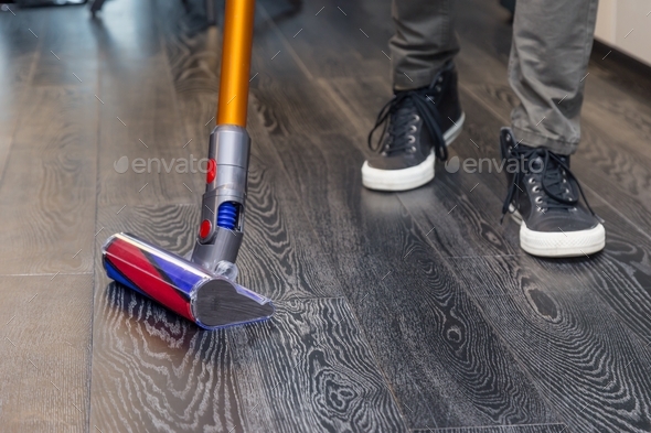 A man vacuums the floor with a compact vacuum cleaner