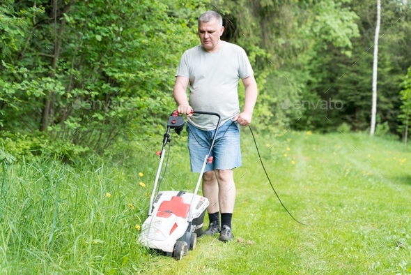 A man mows the grass on the lawn with an electric lawn mower