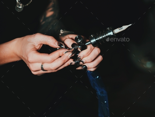 Artist prepares tools and machine for tattoo session, woman holding a tattoo gun