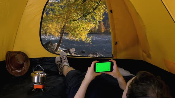 Camper Lies in Open Tent and Using Smartphone with Green Screen, Altai