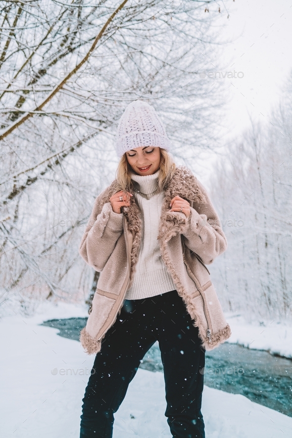 Young trendy woman in winter outfit posing under snowfall near river in  forest. Fashion, lifestyle Stock Photo by Kohanova