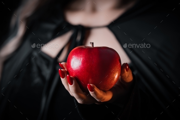 Woman as witch in black coat offers red apple as symbol of temptation, poison. Fairy tale