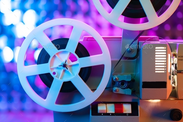 Retro reel with film rotating on colorful shining sparkles wall.  Old-fashioned 8mm film projector Stock Photo by Kohanova