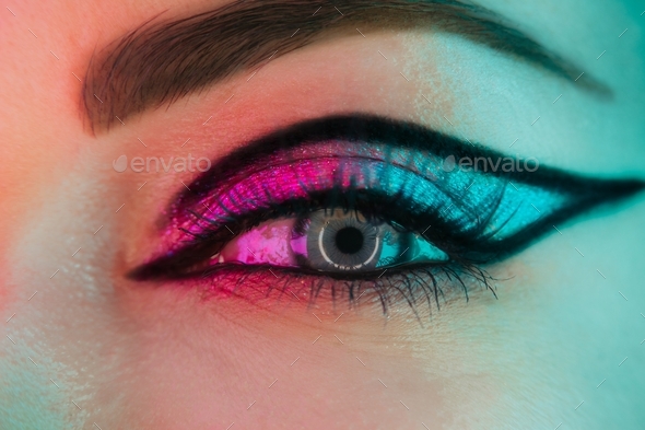 Close up of woman eye with fancy arrow make-up under neon light. Glitter shadows and false lashes.