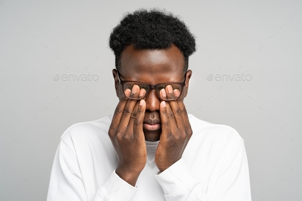 Sleepy young afro-american man in glasses rubbing his eyes, feels tired after working on laptop