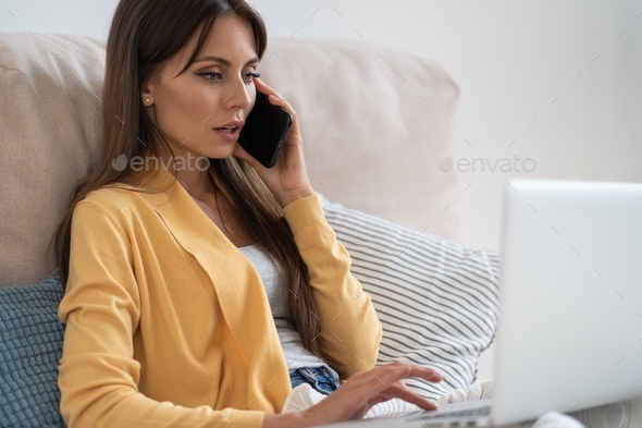 Millennial woman watching educational video course on laptop, talking on mobile phone