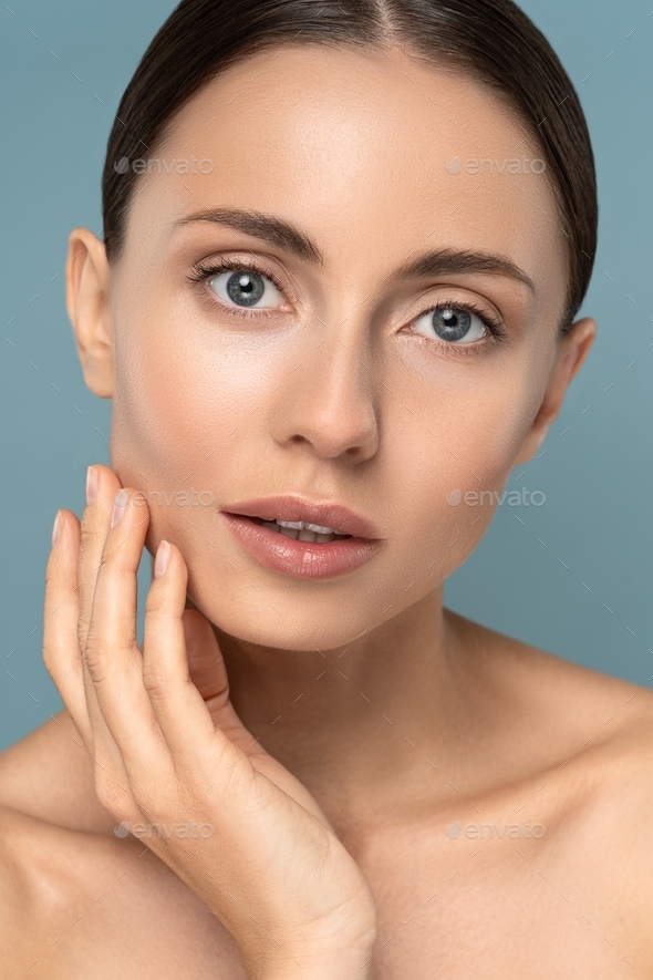 Woman with natural makeup, combed hair, touching her well-groomed pure skin on face. Facelift.