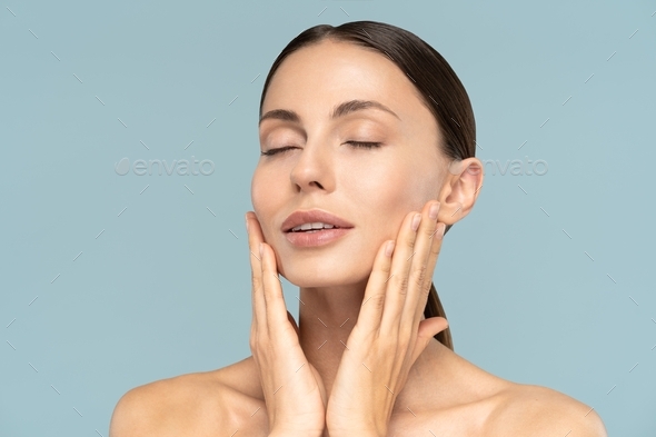 woman with natural makeup, combed hair, touching well-groomed pure skin on face, closed eyes
