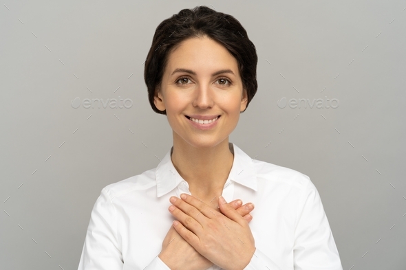 Friendly woman holds hands on chest, feels grateful for love, appreciation, thankful and support