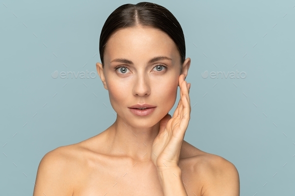 Woman with natural makeup, combed hair, touching well-groomed pure skin on face. Beauty, facelift