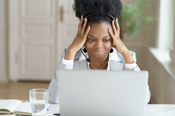 Angry annoyed afro businesswoman screaming, wear headphones talking to a bad customer work on laptop