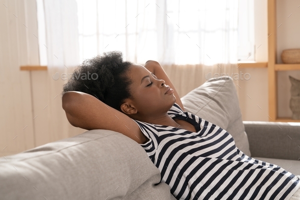 African American woman wear stripped t-shirt sleeping on couch with arm under head at home. Rest.