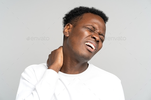 Unhappy Black man suffering from neck pain, pinched nerve in her back, has spinal problem. Studio.