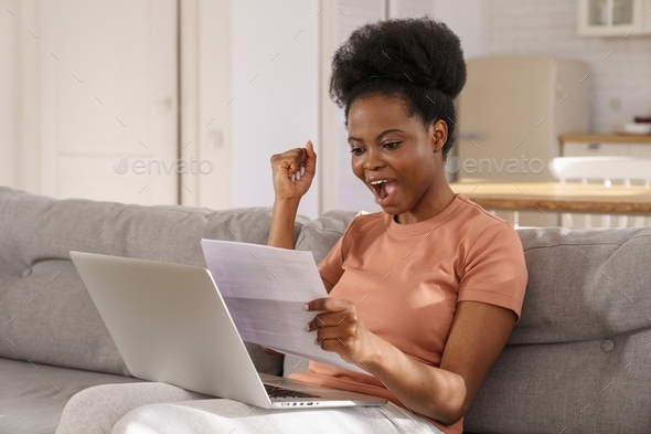 Excited Black woman sit on sofa at home receiving job enjoy exam results or college admission letter