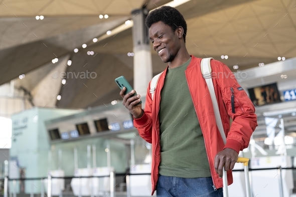 Happy black man in airport terminal use smart phone to book hotel, call taxi after flight arrival