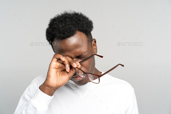 Exhausted Black man take off glasses rubbing his eyes feels tired after work on laptop. Overwork.