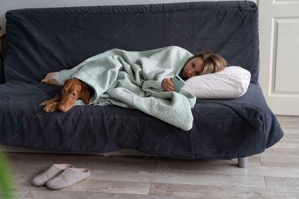 Sad woman lying on sofa with dog, using smart phone wait for boyfriend call or text, feels depressed
