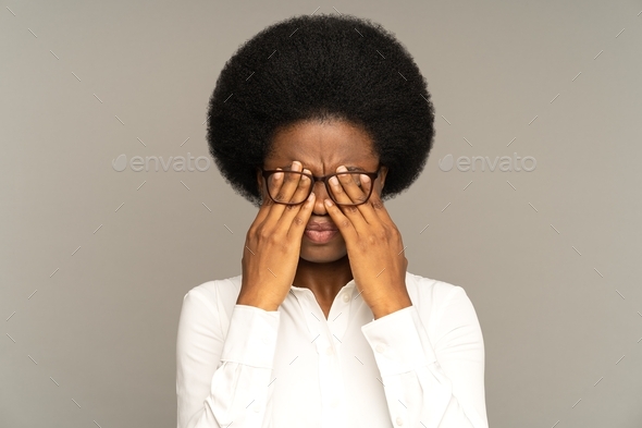 Exhausted afro female feels tired, rubbing eye after work. Fatigue, overwork, computer.