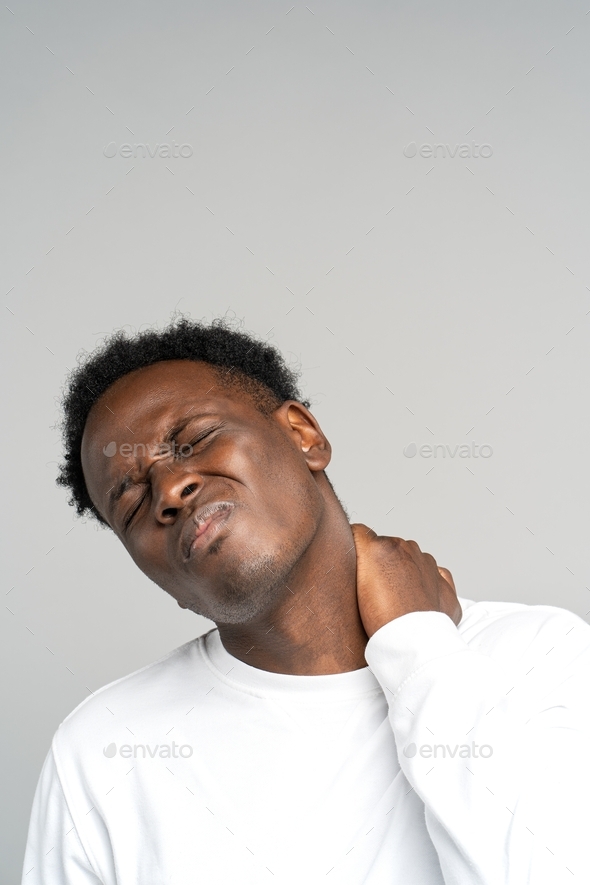 Unhappy Black man suffering from neck pain, pinched nerve in her back, has spinal problem. Studio.